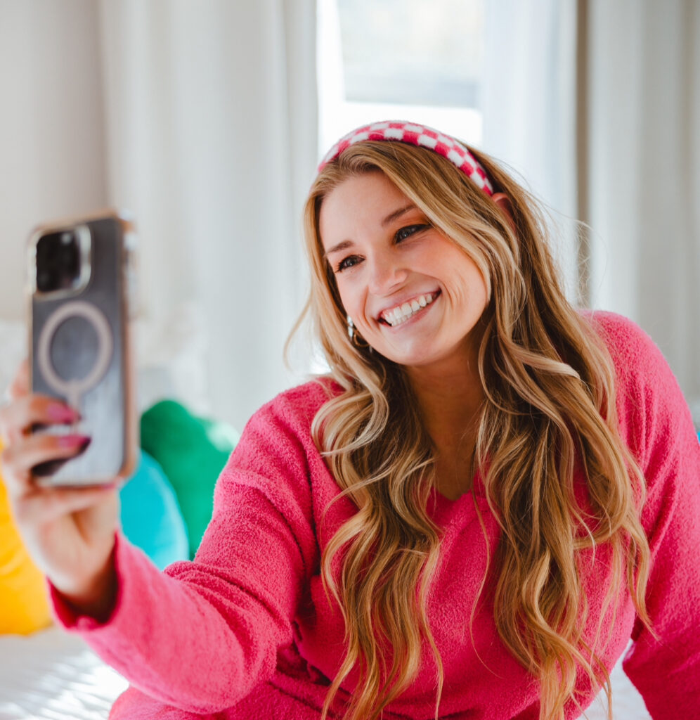 social media strategist sydney simpson pink shirt holding phone smiling blonde girl